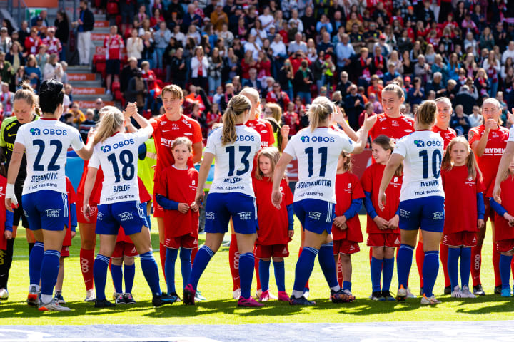 Bilde av to damelag som håndhilser på hverandre ute på en solrik fotballbane.