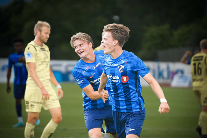 En gruppe jenter i stabæk fotballdrakt som løper på rekke ut på fotballbanen mens supportere tar hight five med dem.