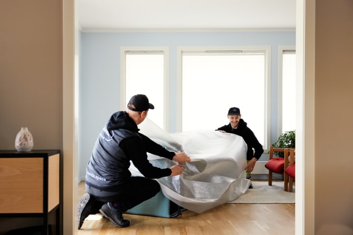 To menn med caps pakker inn en sofa som de henter fra en stue.