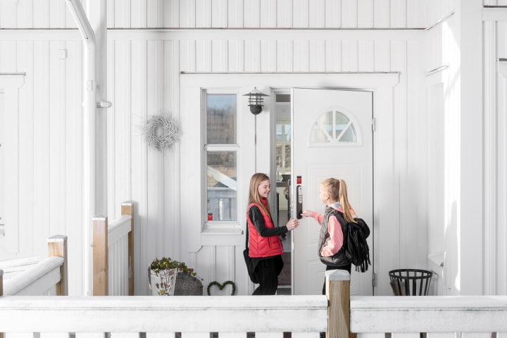 To jenter låser opp koden på døra som er koblet til alarmen. Det er et hvitt hus.