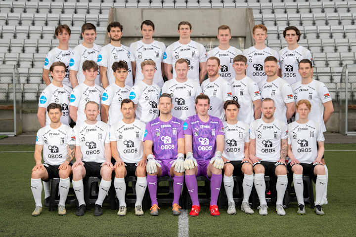 Oppstilt lagbilde med 25 mannlige fotballspillere som ser seriøst mot kameraet.