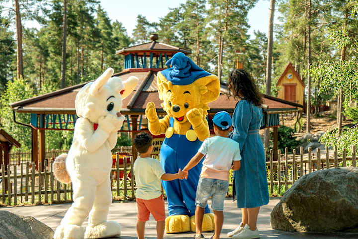 En utkledd som bamse o kanin hilser og leker med to barn og en voksen.