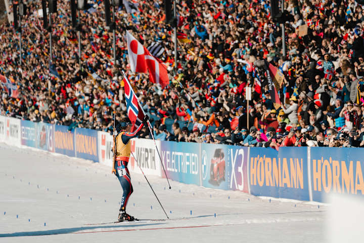 En skiskytter feirer foran publikum etter å ha passert målstreken.