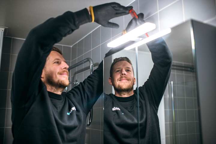En mann fikser belysning på speilet på badet. Han smiler.