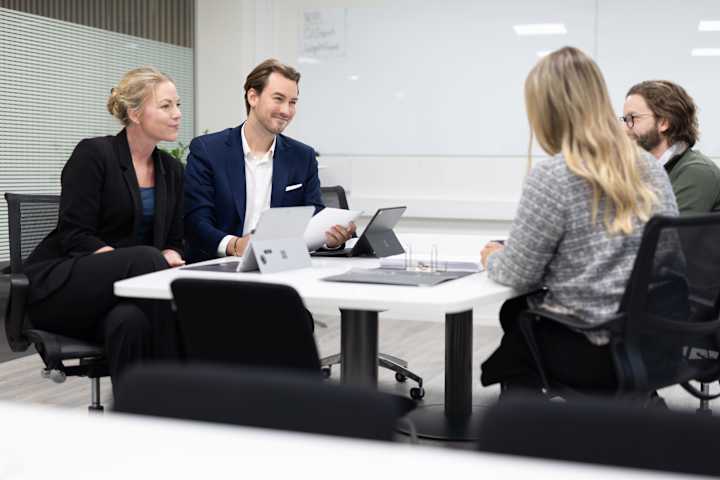 Fire mennesker sitter rundt et bord. To av dem er advokater og hjelper paret. De smiler og har ipader foran seg.