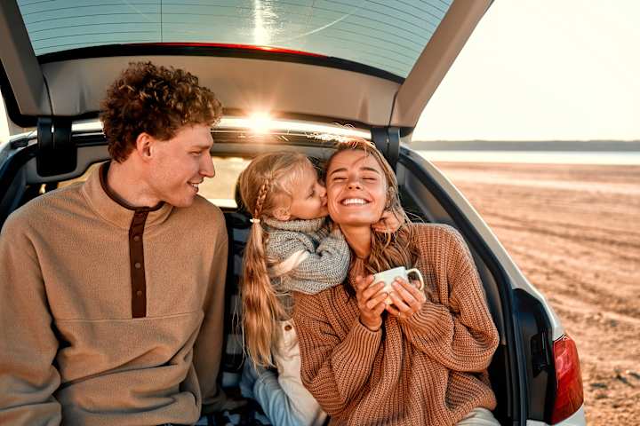 Far bærer barn ut av bilen. Mor og bror er på vei ut av bilen