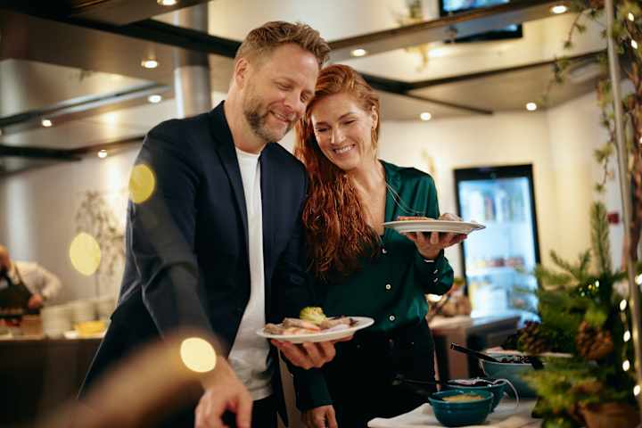 En mann og en kvinne tar seg julemat om bord på Go Nordic Cruiseline. De smiler ved en buffet.