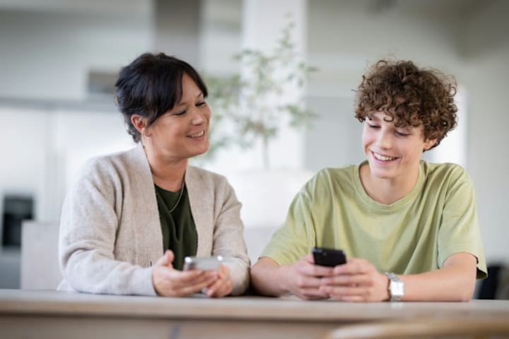 En mann sitter med en grønn skjorte og taster på mobilen, han smiler.