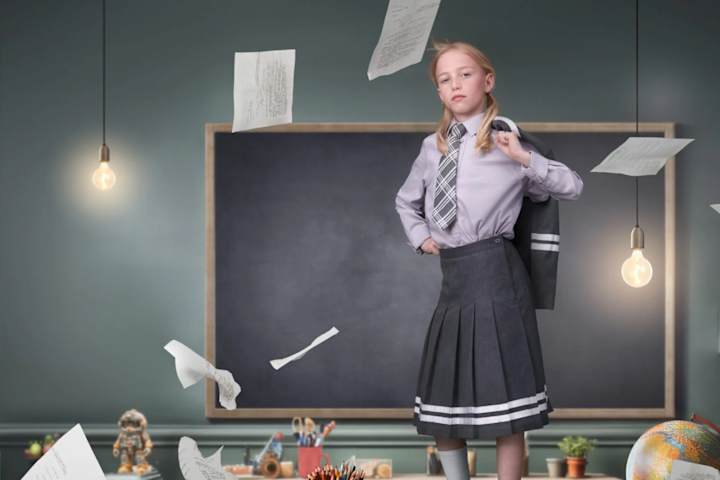 Matilda står på pulten til læreren med blazeren over skulderen.