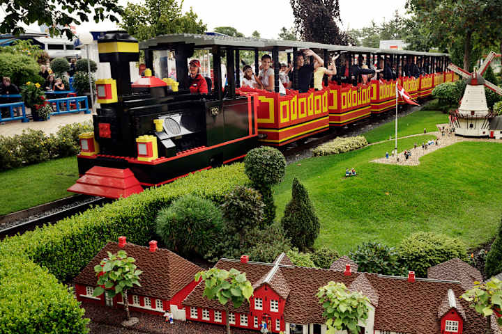 Tre jenter står samlet og smiler mot legohusene i Miniland i Legoland.