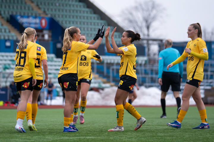Foto av seks kvinnelige fotballspillere for Lillestrøm fotballklubb som er samlet på banen. To av dem tar high five.