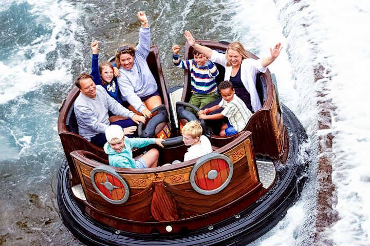 Voksne og barn sitter i en karusell i vannet og har henda i været. De smiler og har det gøy.