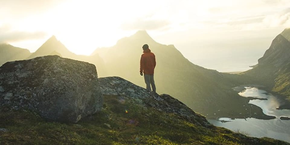 En person skuer utover fjellene i solnedgang.