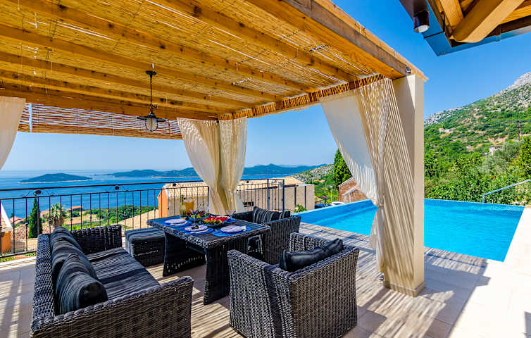 Terrasse med sofalounge, pergola, badebasseng og utsikt mot havet.