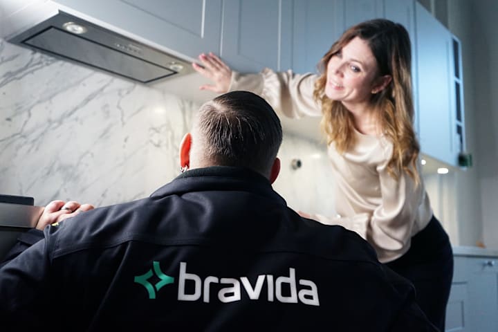 En mann fra Bravida skal fikse en komfyr. En kvinne står over og viser. Hun har langt hår og smiler.