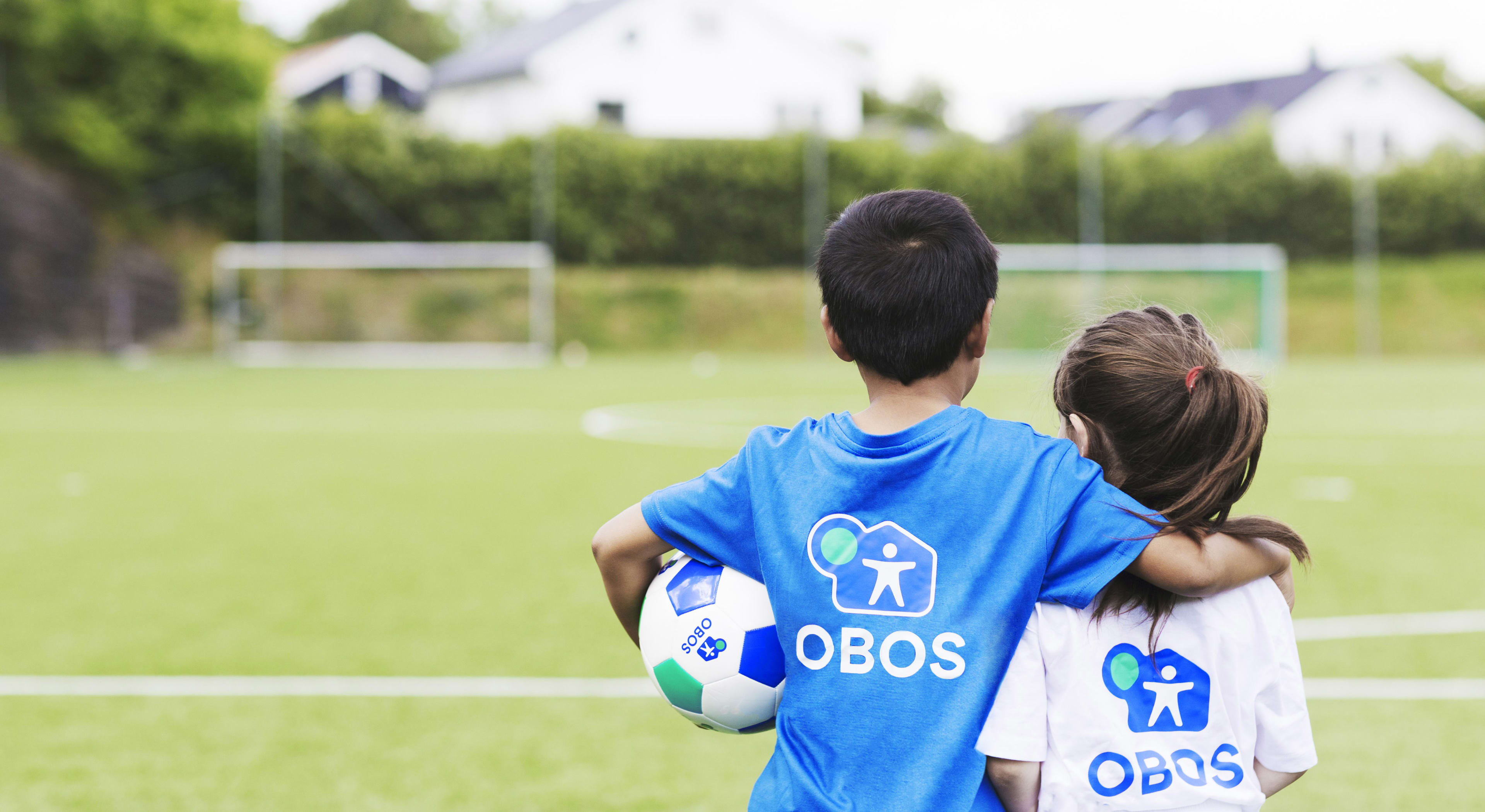 To barn i OBOS-tskjorter som ser mot et fotballmål