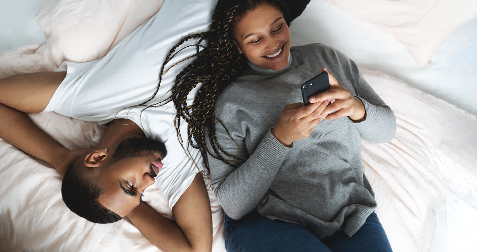 Ungt par som ligger i senga og er på telefonen