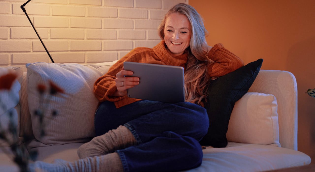 Kvinne sitter i en sofa og ser på en pad