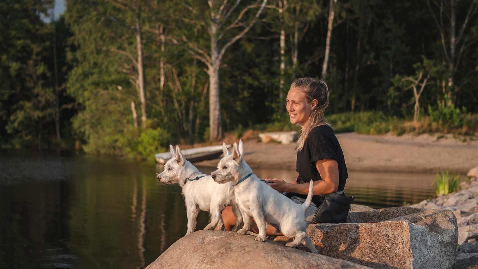 kvinna och två hundar sitter vid sjö