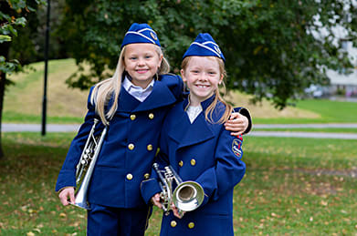 To jenter med korpsuniform og instrumenter smiler på et bilde sammen