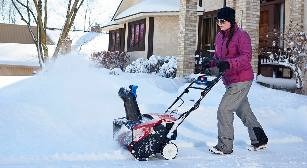 Kvinne som bruker en snøfreser. Det er vinter og mye snø ute