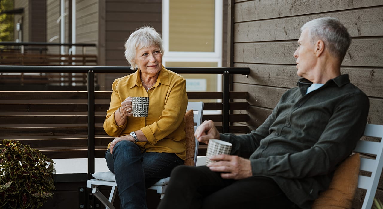 En mann og en dame sitter utenfor huset sitt og drikker kaffe