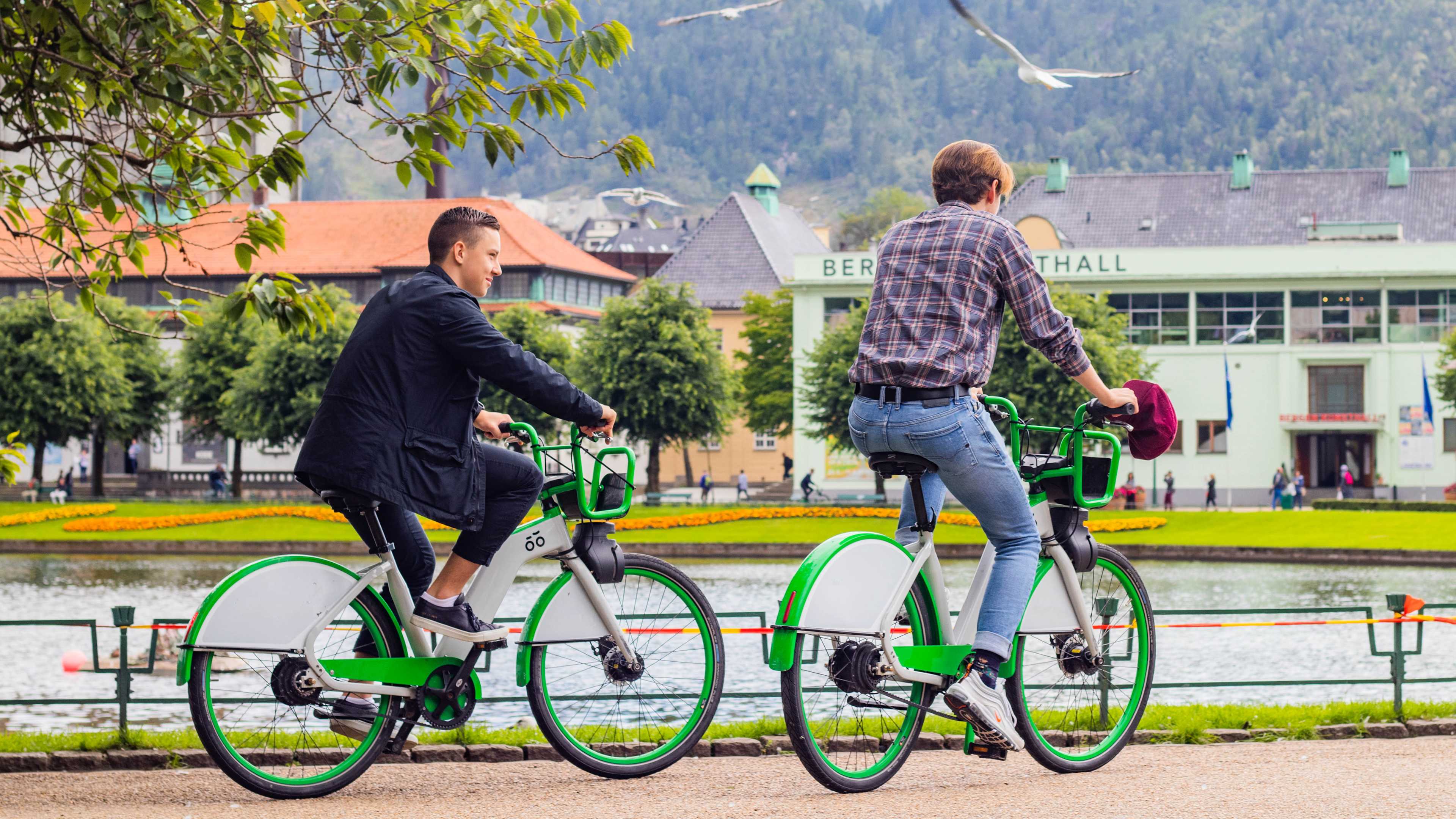 Foto av to gutter i Bergen sentrum som syker rundt på grønne bysykler.