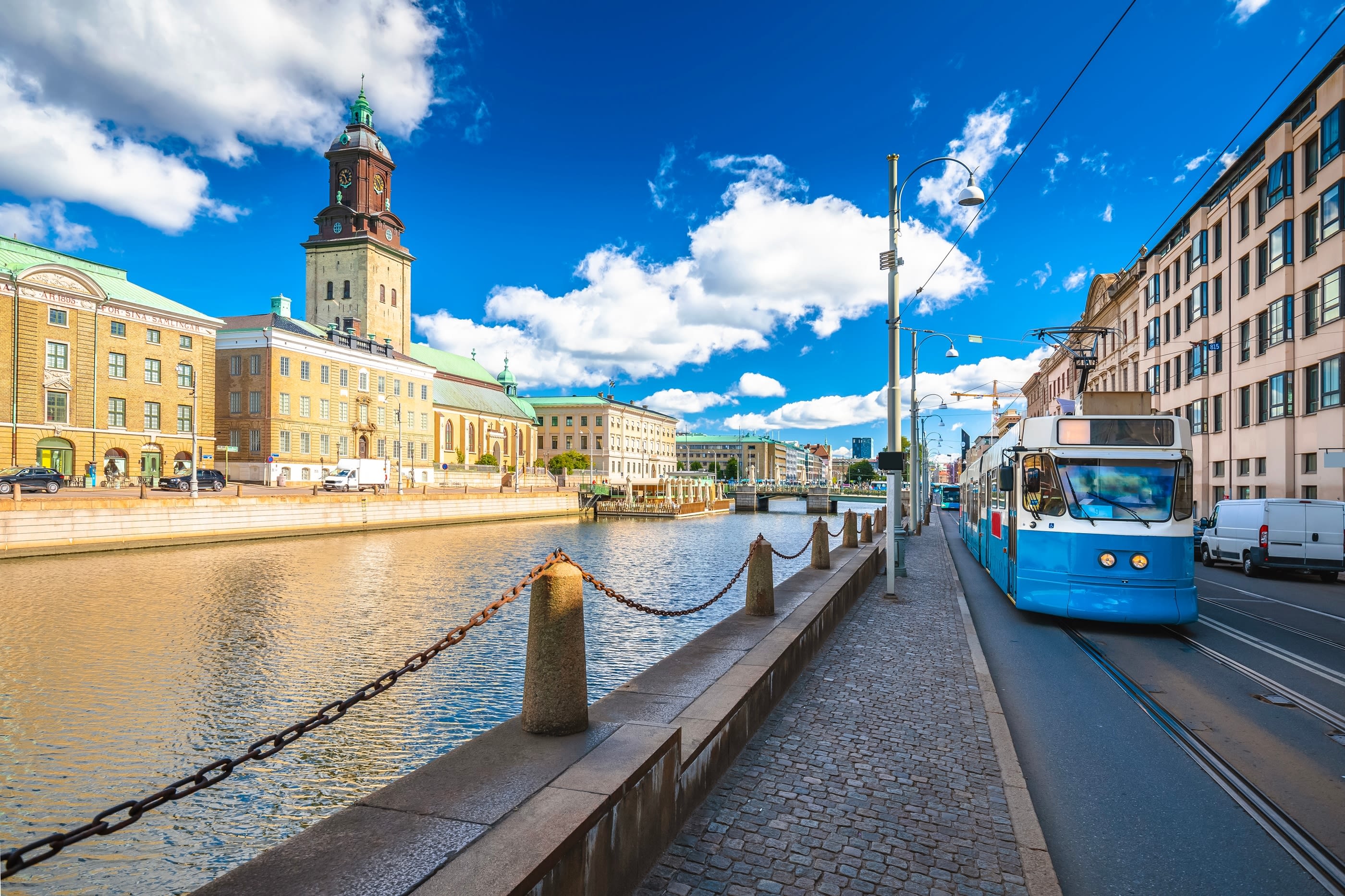 En blå trikk kjører ved elva i Gøteborg. Vakre bygninger ved siden av.