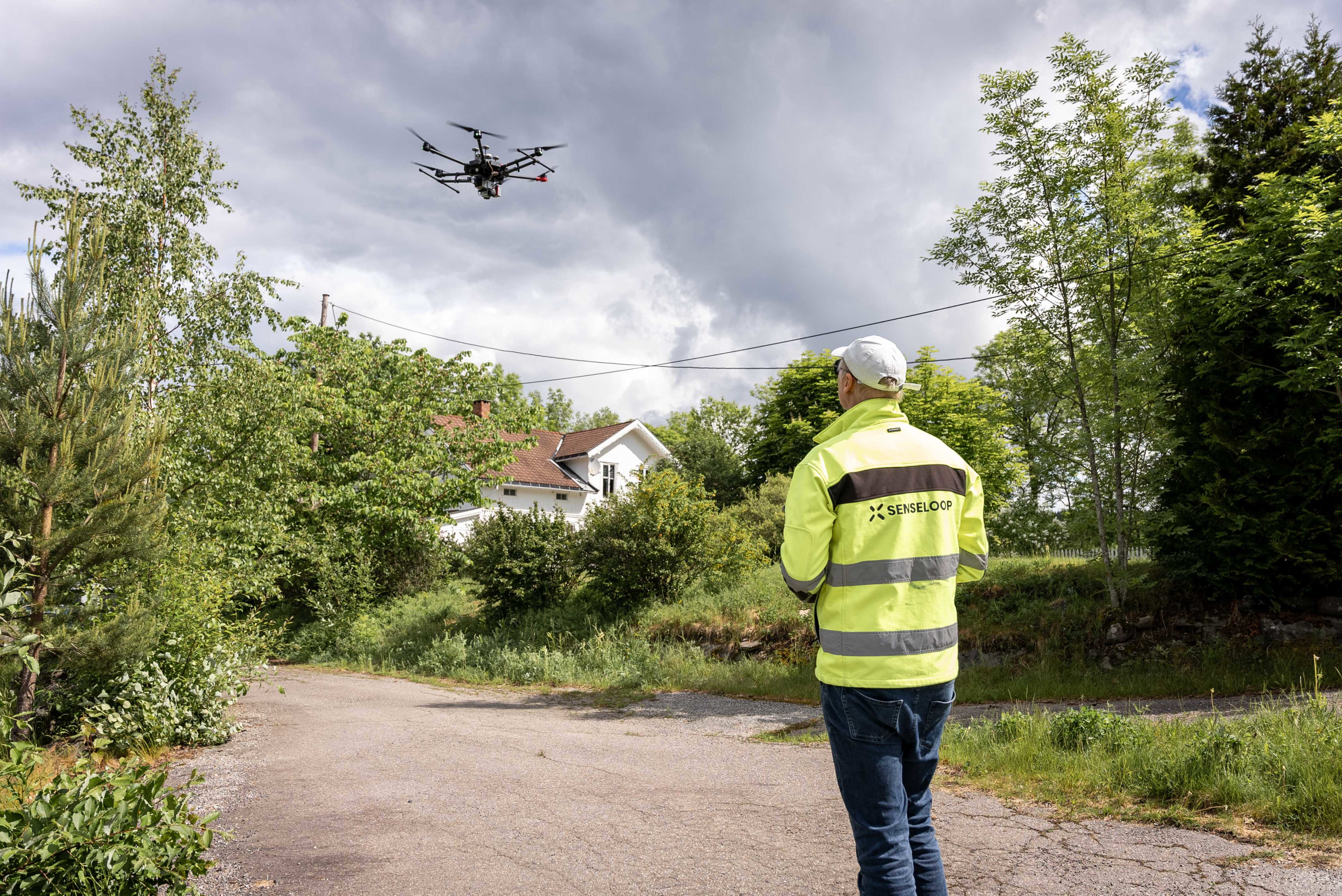 Mann med gul jakke med Senseloop-logo på ryggen styrer en drone