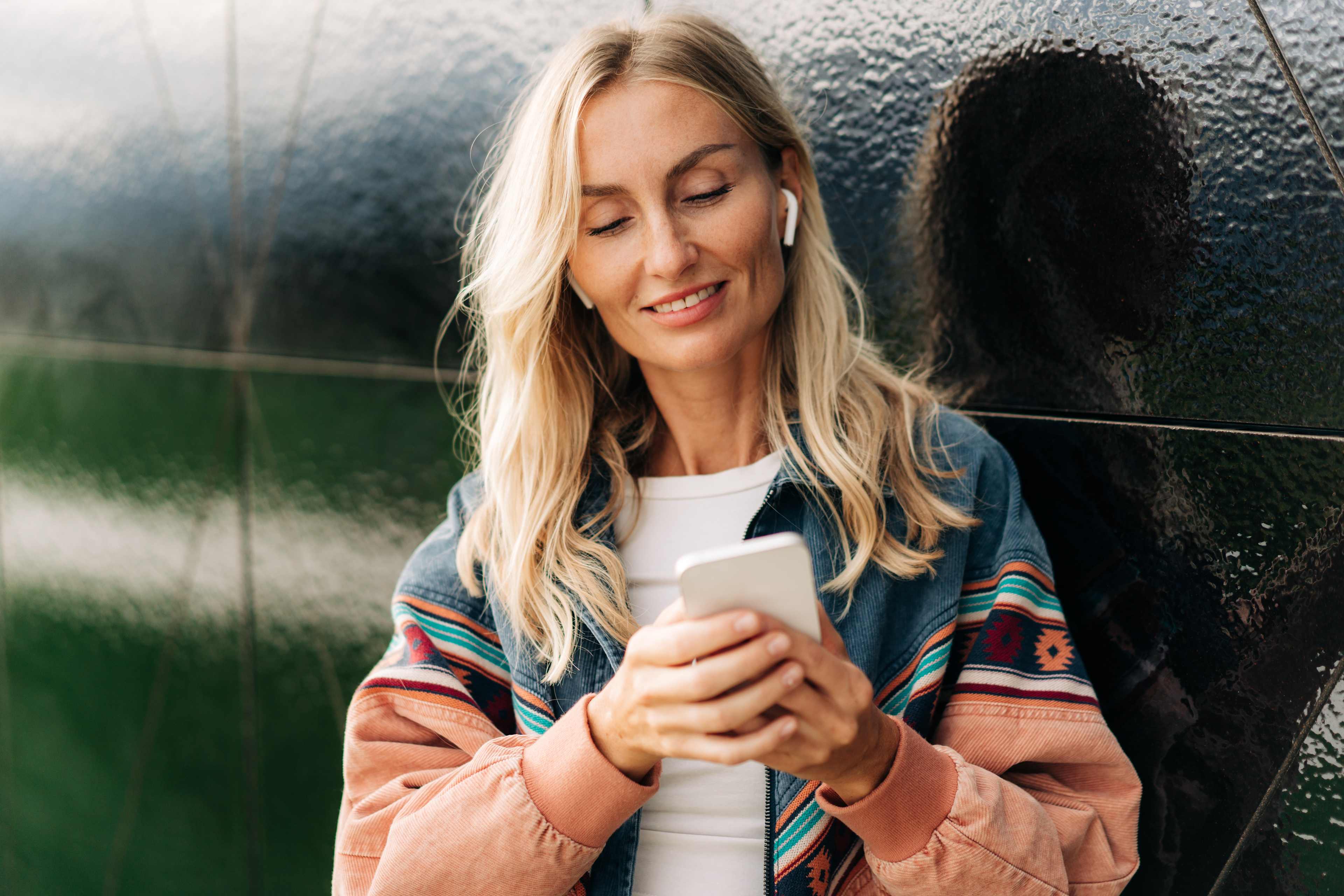 Ung kvinne ser på telefonen og bruker Apple AirPods 4