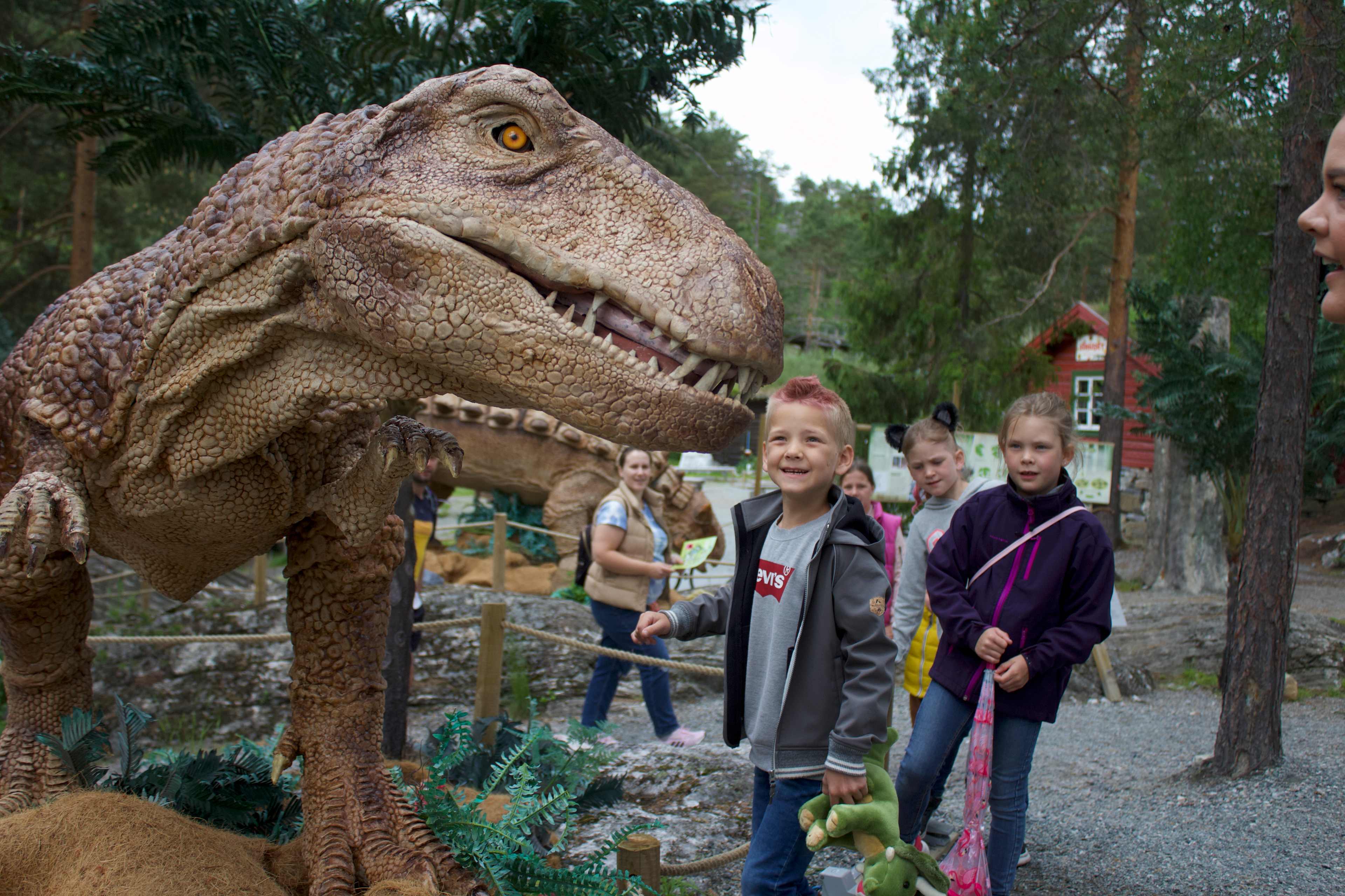 Enn gutt ser på en utstoppet dinosaur. Flere barn ser på. De synes det er gøy. 