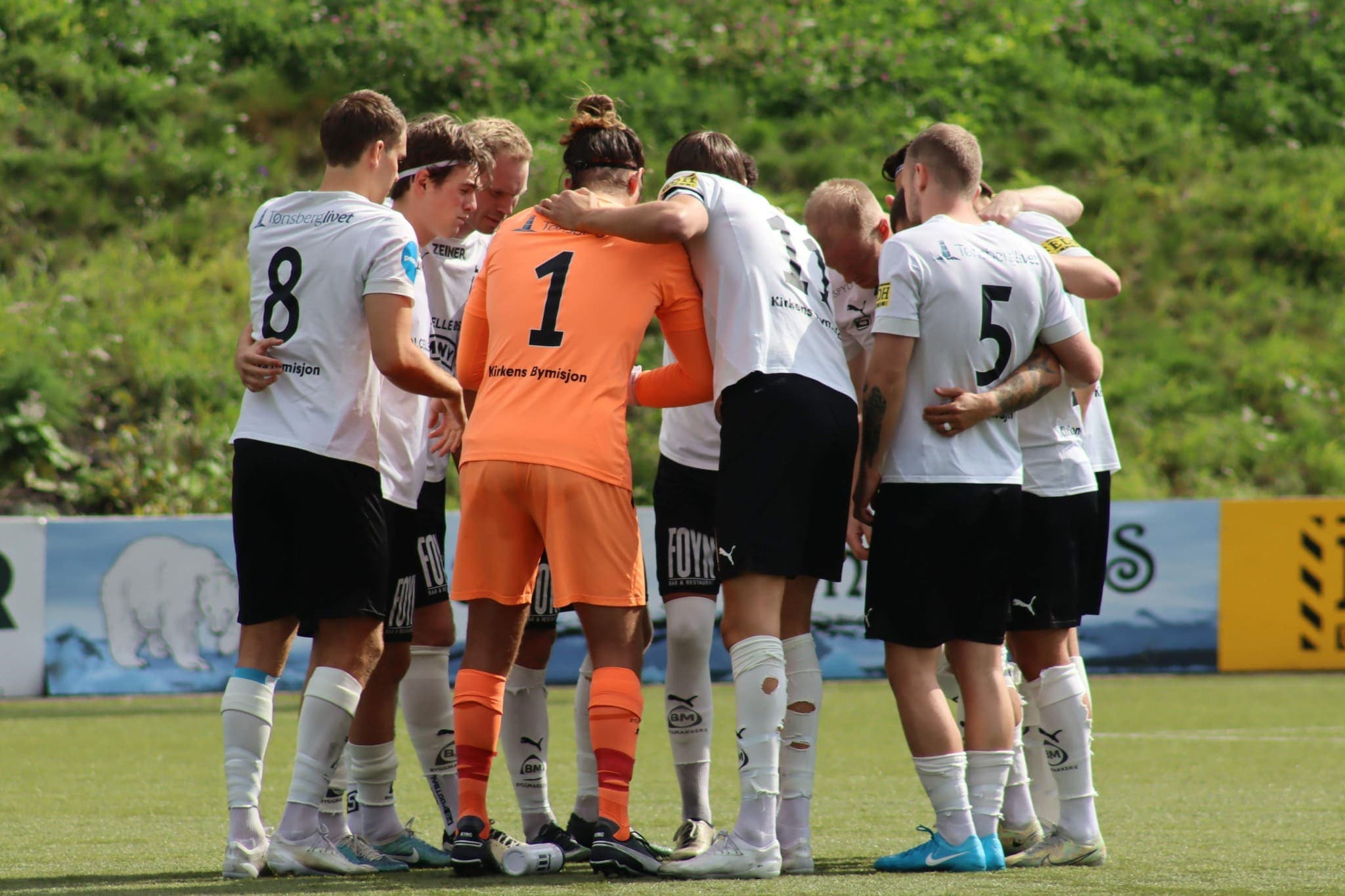 Foto av en gjeng mannlige fotballspillere som samler seg i sirkel før kampstart.