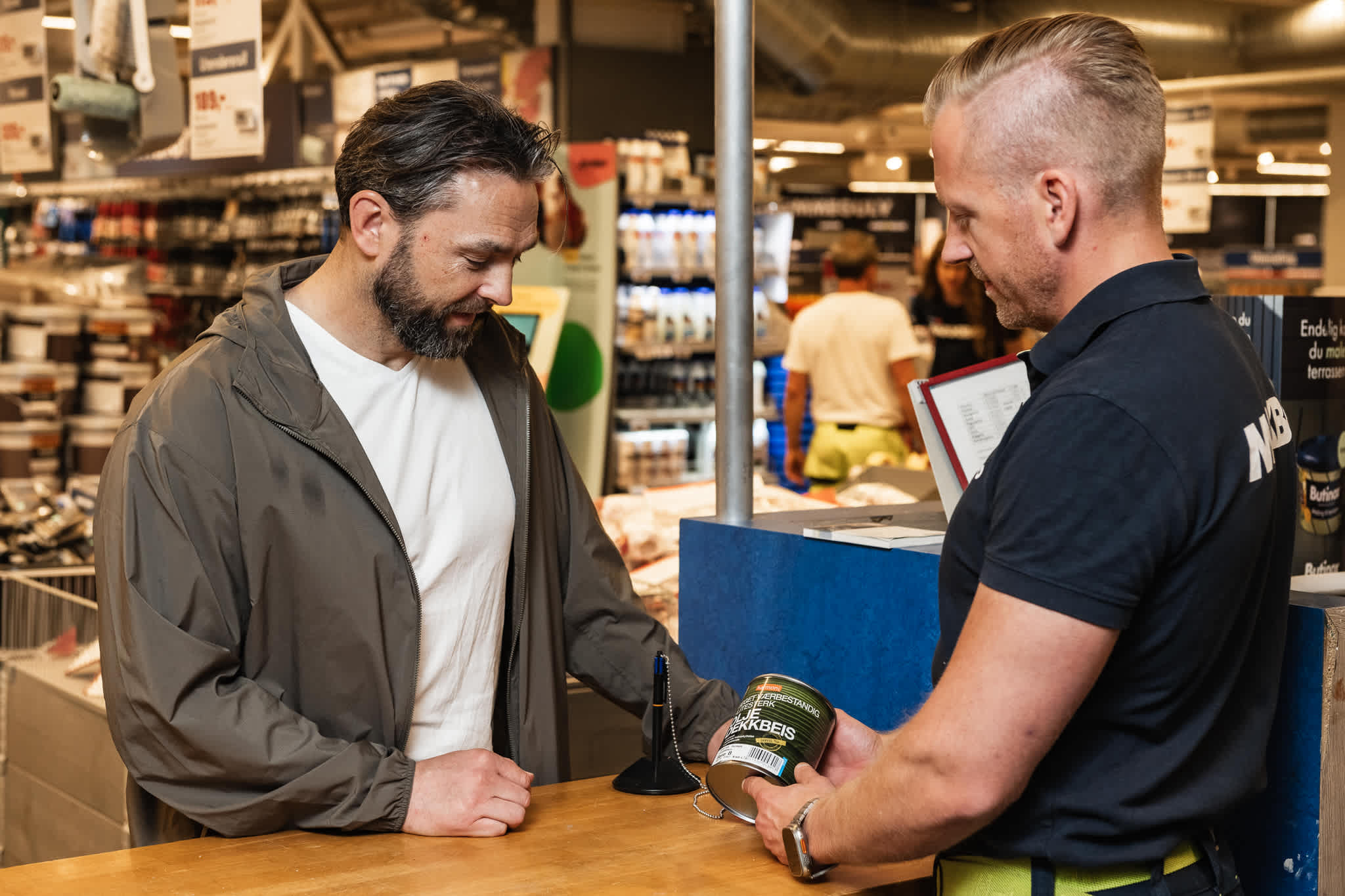 En mannlig ansatt på Maxbo hjelper en mann med fargevalg på beis.