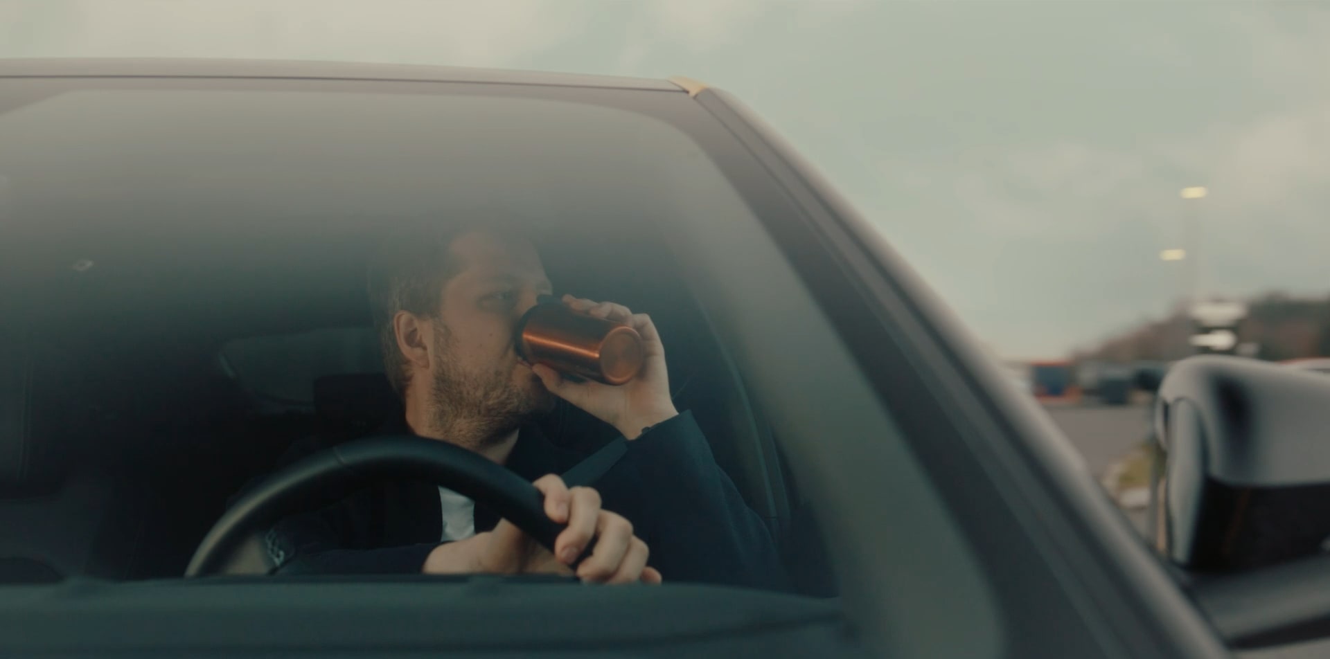En mann kjører bil og drikker av en Koppen som tilhører Circle K.