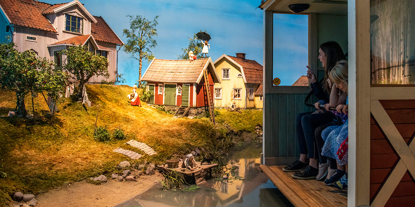 Bilde fra Junibacken. Mennesker sitter i en vogn og blir kjørt bortover for å se ulike hus og historier. 