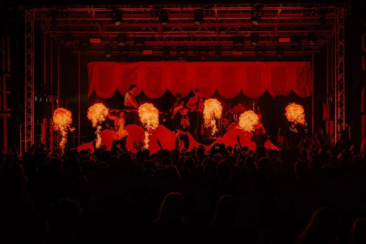 Scenen på Spirefest. Det er mørkt og det kommer flammer fra scenen. I forgrunnen ser vi konturene av publikum med hender i været.