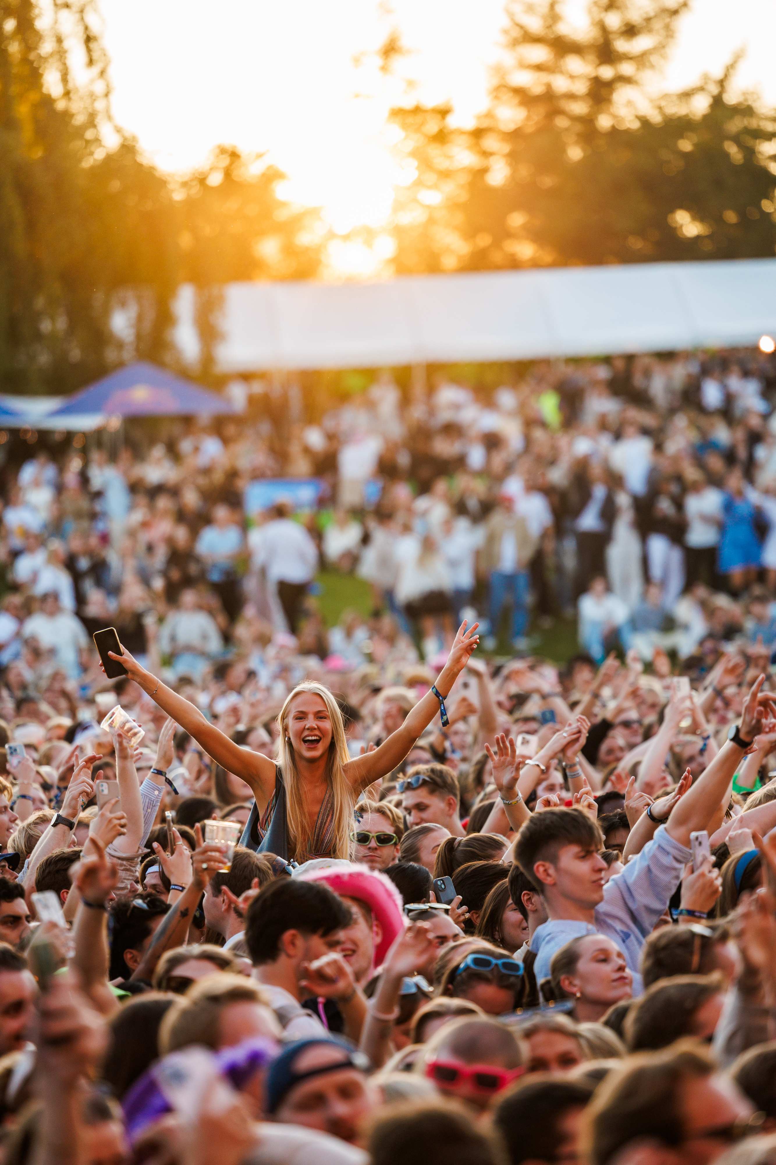 Publikum med hender i været på Festningen festival. Vi kan skimte solnedgangen i bakgrunnen.