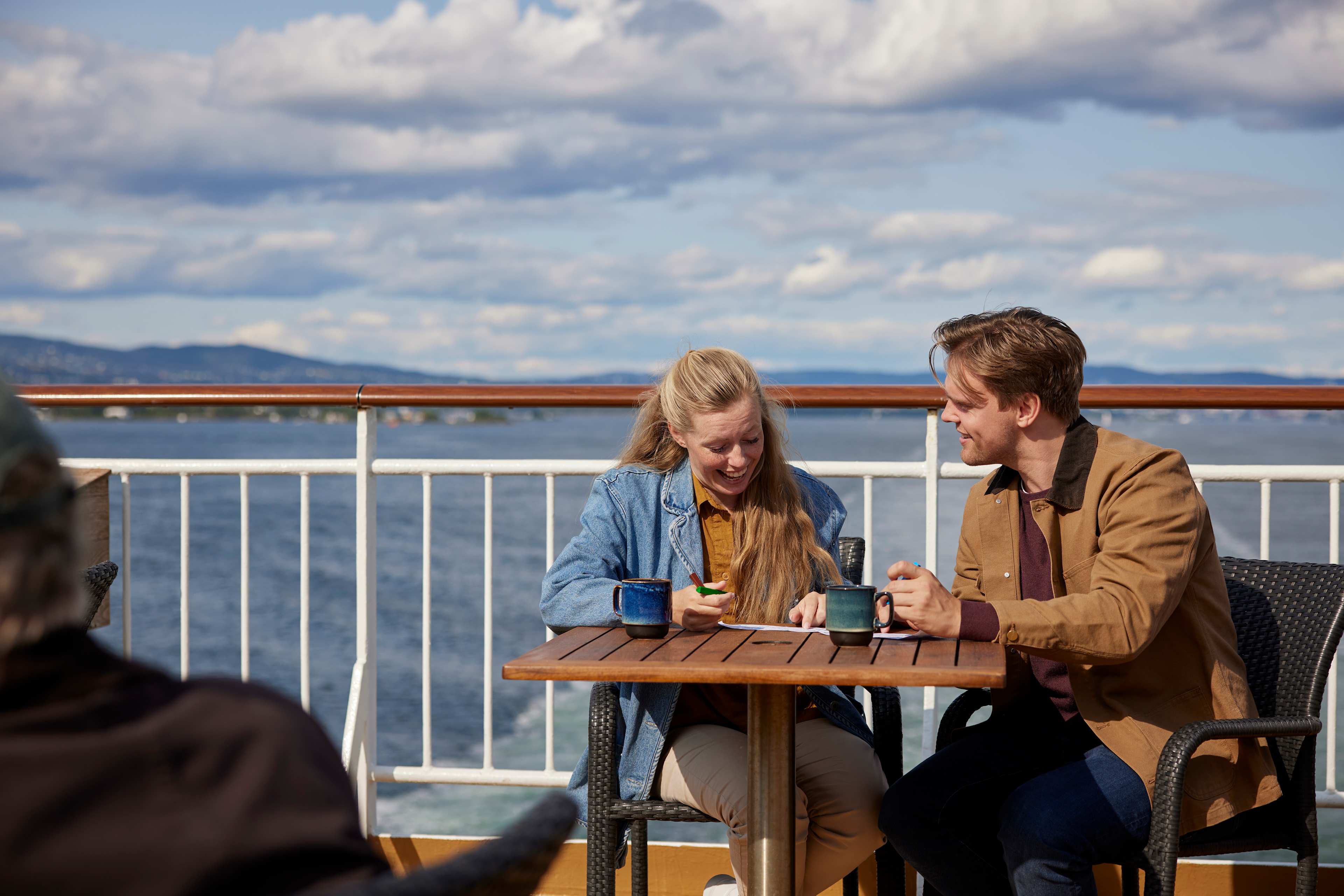 Et par sitter ute på dekk om bord på Go Nordic Cruiseline. De smiler og planlegger.