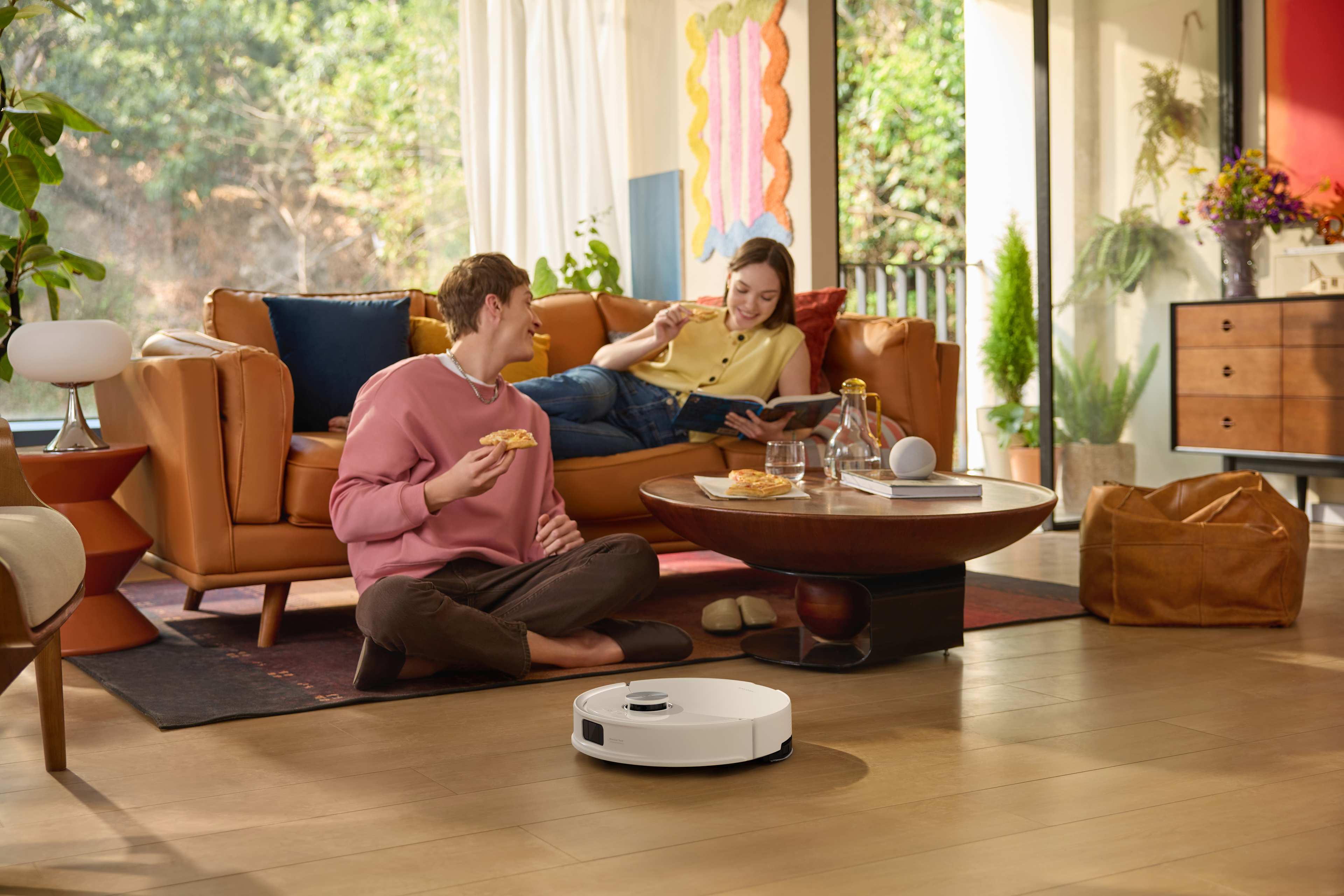 Et par spiser pizza og ligger i sofaen mens robotstøvsugeren rengjør.