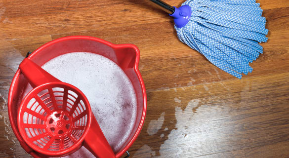 En rød vaskebøtte med såpevann og en blå mopp på et tregulv