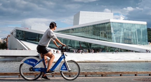 Kvinne på en bysykkel med Operaen i bakgrunnen