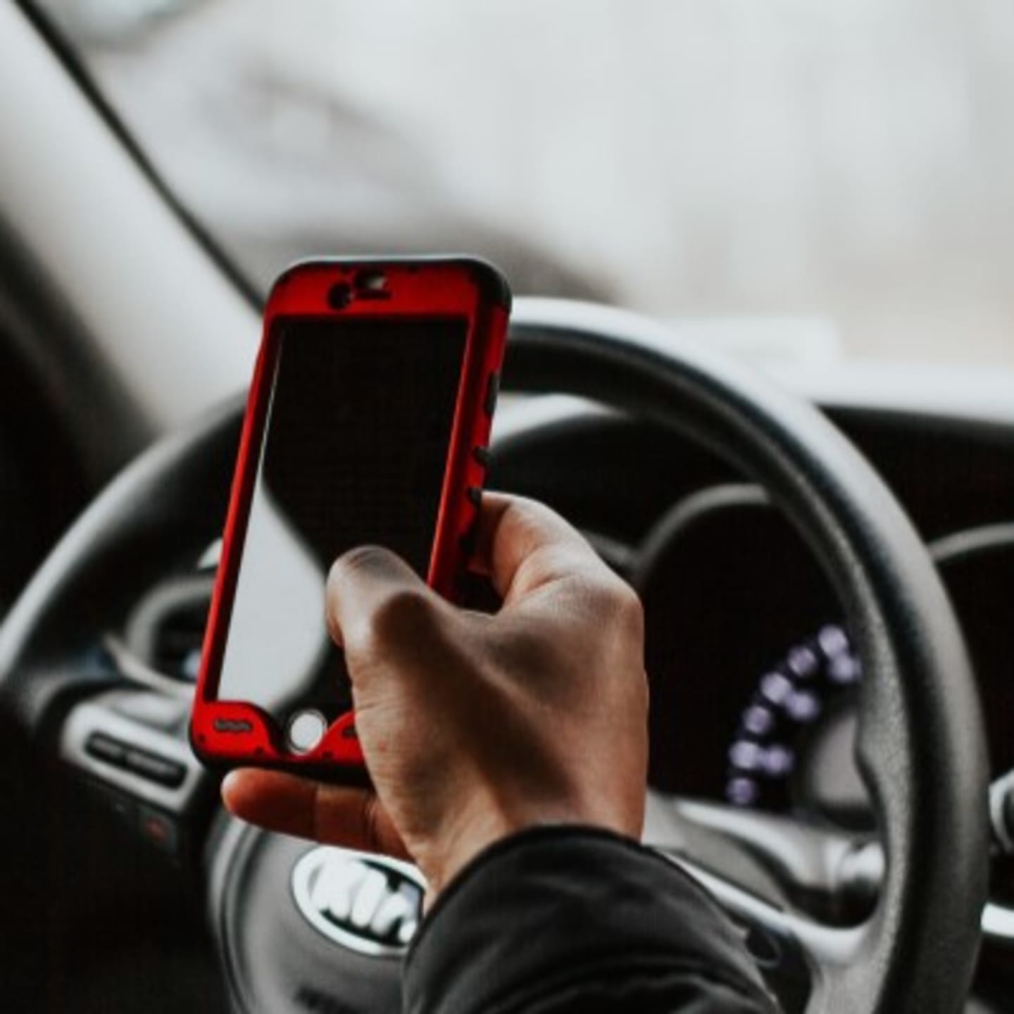 En person holder en mobil mens hen er bak rattet. Foto.
