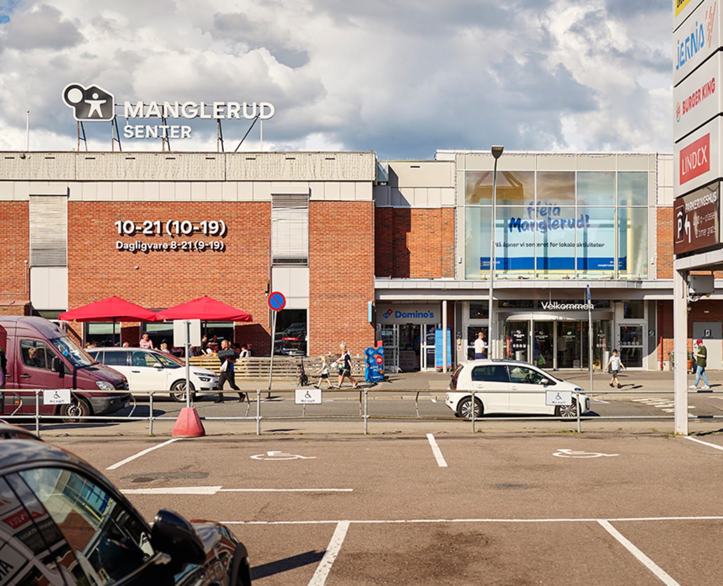 Foto av fasaden og inngangspartiet til Manglerud Senter, samt et stykke av parkeringsplassen til senteret.