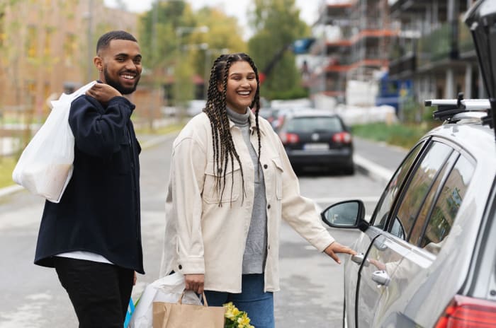 Smilende mann og dame med handleposer på vei inn i bilen