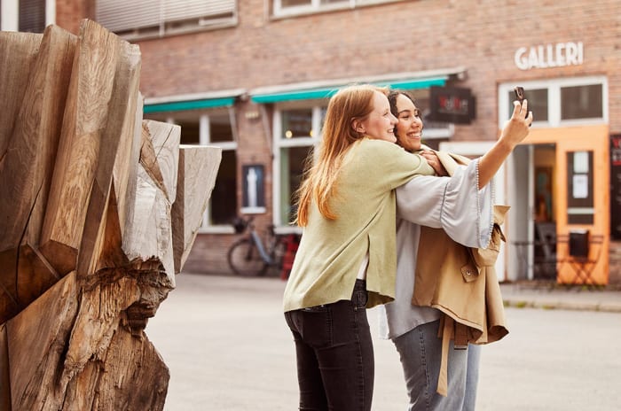 Jenter som tar selfie foran treskulptur i Kulturgaten på Fornebu