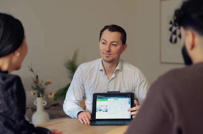 Henry Ryberg Pedersen sitter og snakker med to mennesker og holder i en ipad.