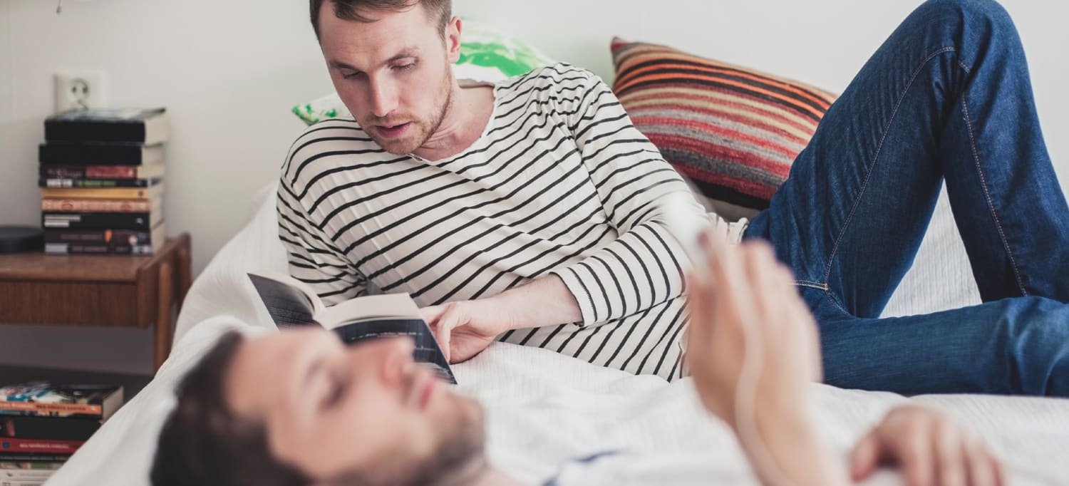 Två män som ligger på en säng med mobil och hörlurar OBOS