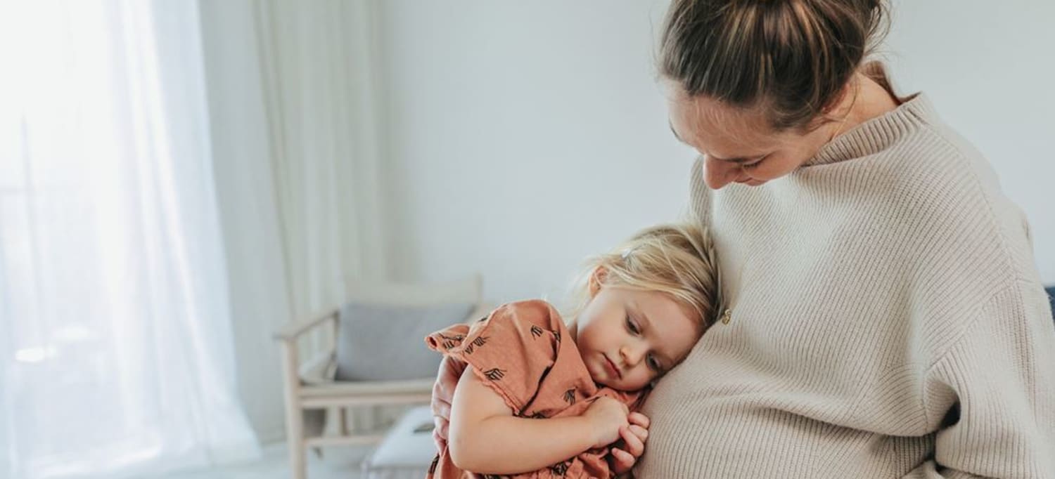 Gravid mamma sitter med dotter i knä