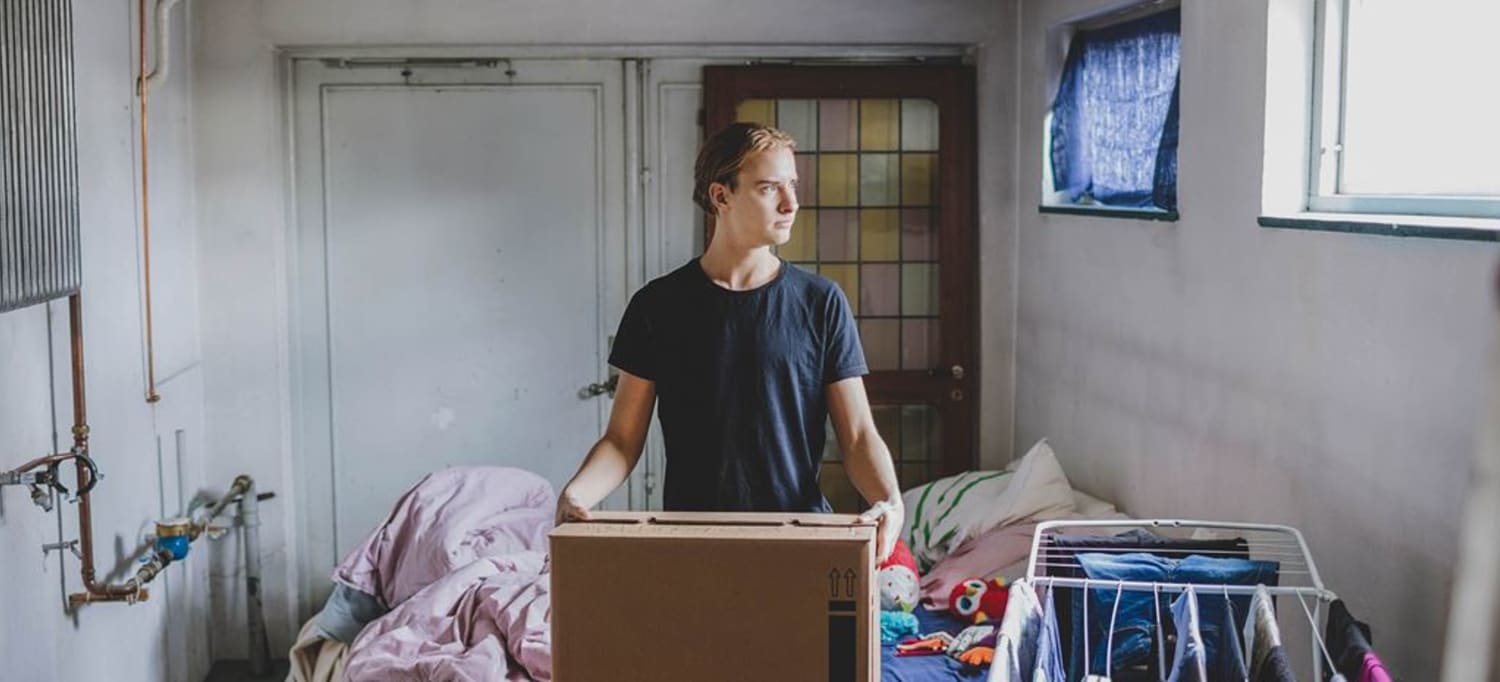 En man står och håller i flyttkartong i ett ljust källarrum.