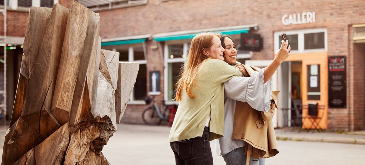 Jenter som tar selfie foran treskulptur i Kulturgaten på Fornebu